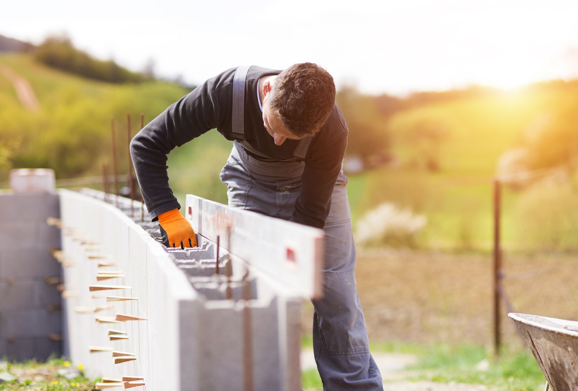 Un ouvrier du bâtiment ganté utilise un niveau pour vérifier l'alignement d'un mur en parpaings.