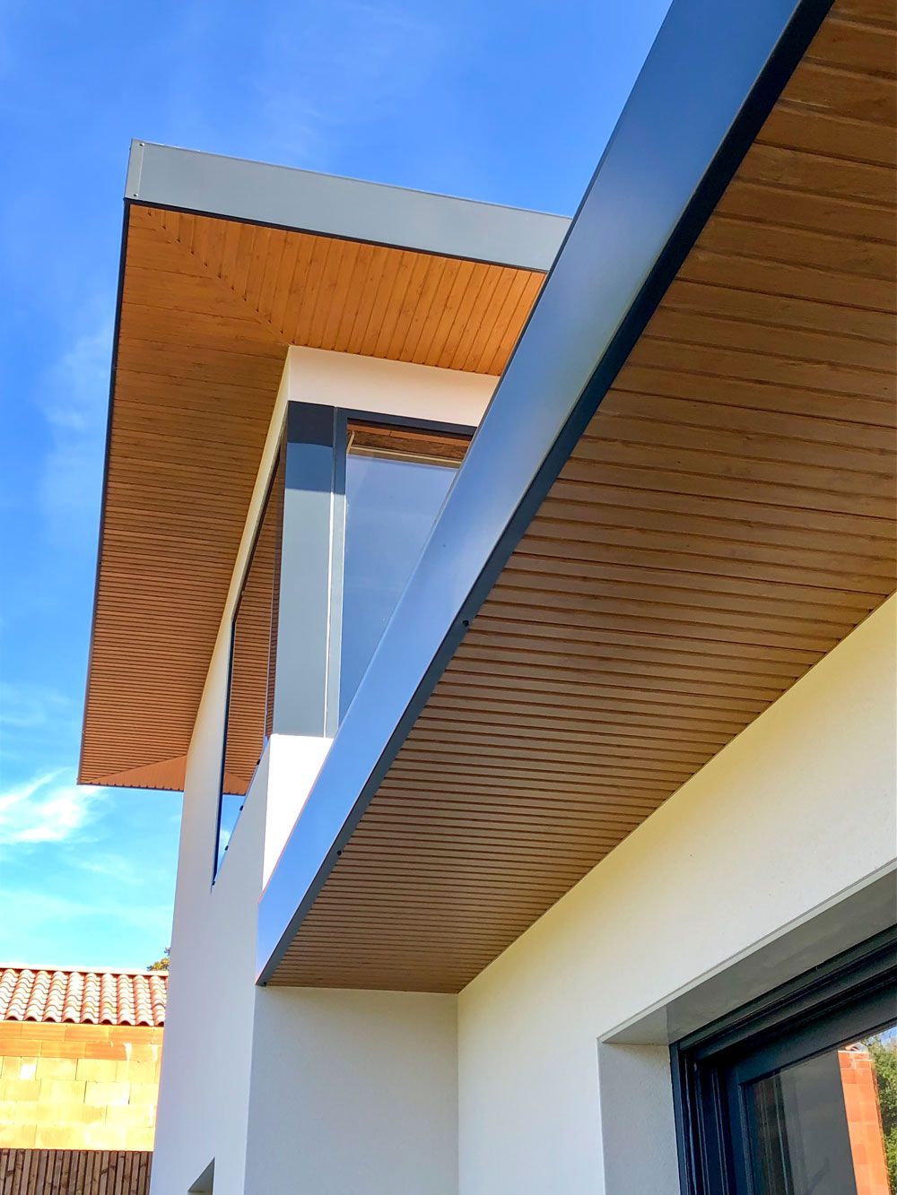 Extérieur d'une maison moderne caractérisée par un toit plat et pointu en avant-toit avec des soffites lambrissés.