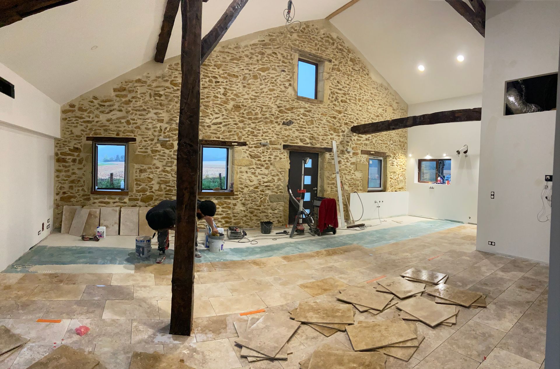 Une personne travaille à la pose du revêtement de sol dans une pièce rustique aux murs de pierre, en construction.