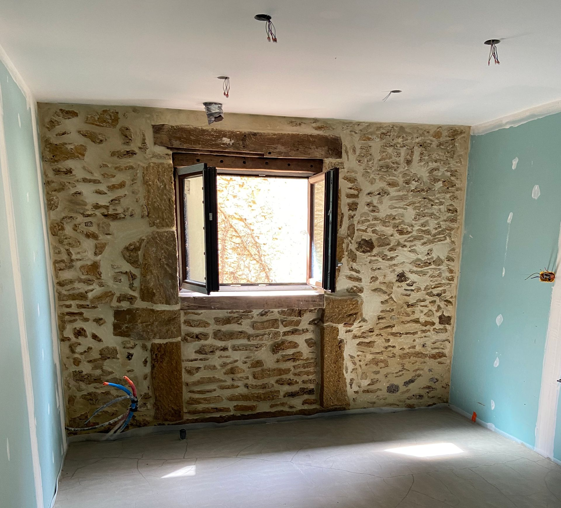 Une pièce en rénovation avec un mur en pierre apparente percé d'une fenêtre.