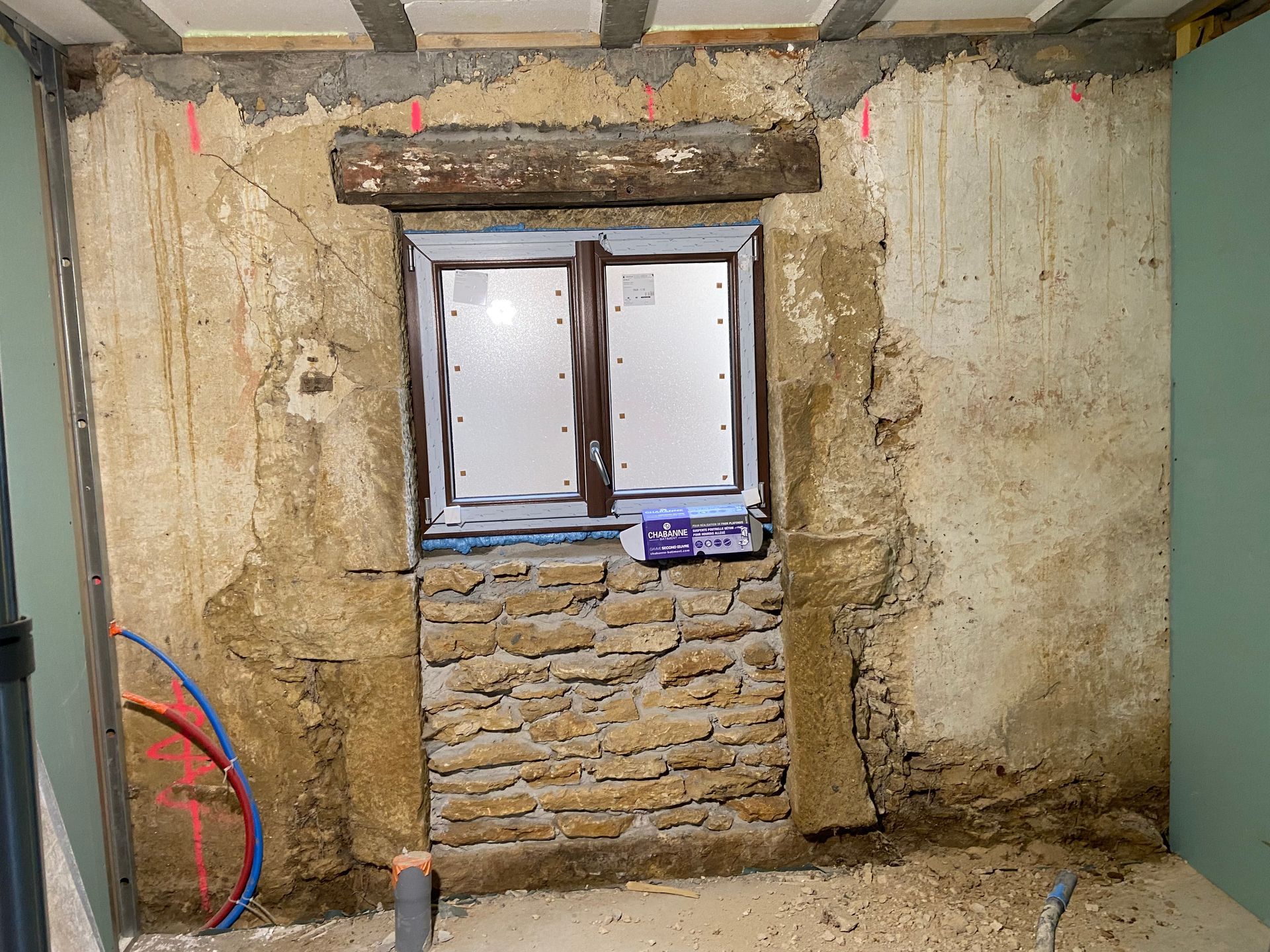 Une fenêtre dans un mur de pierre rustique en cours de réparation, avec maçonnerie apparente.