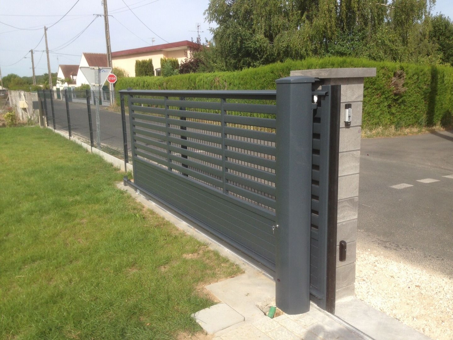 Un portail coulissant à lames horizontales gris foncé, installé sur un pilier en pierre.