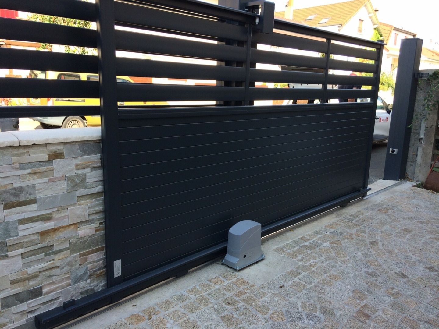 Un portail coulissant moderne en métal noir sur une allée résidentielle.