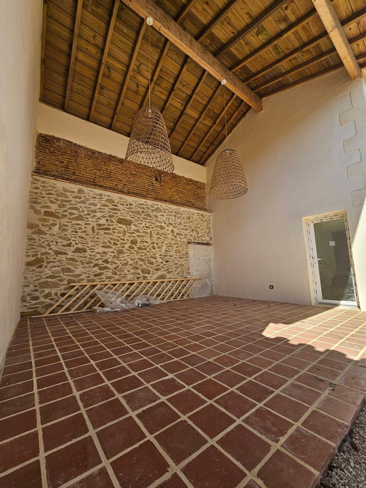 Un patio intérieur doté d'un haut plafond incliné en roseaux, d'un mur en pierre, d'un sol carrelé en terre cuite.