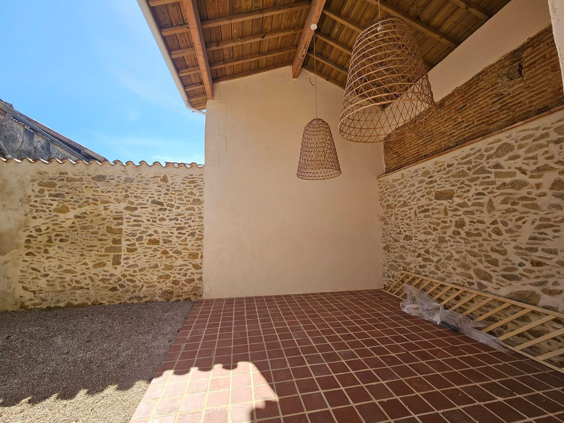 Un espace extérieur partiellement couvert avec des murs en pierre rustique et un sol en carrelage rouge.