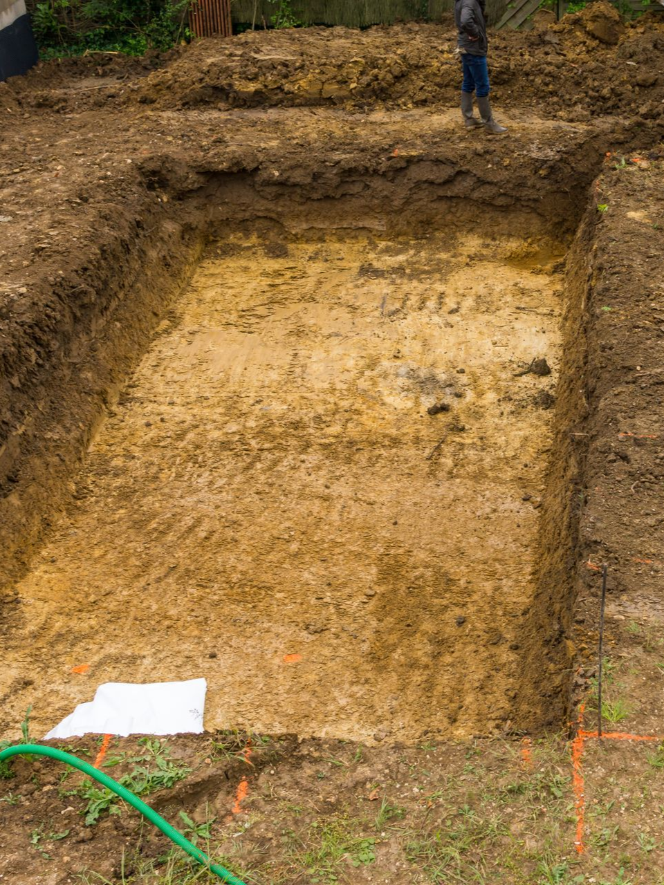 Une fosse d'excavation de fondation rectangulaire dans un sol brun, prête à être construite, marquée avec de la peinture en aérosol orange.