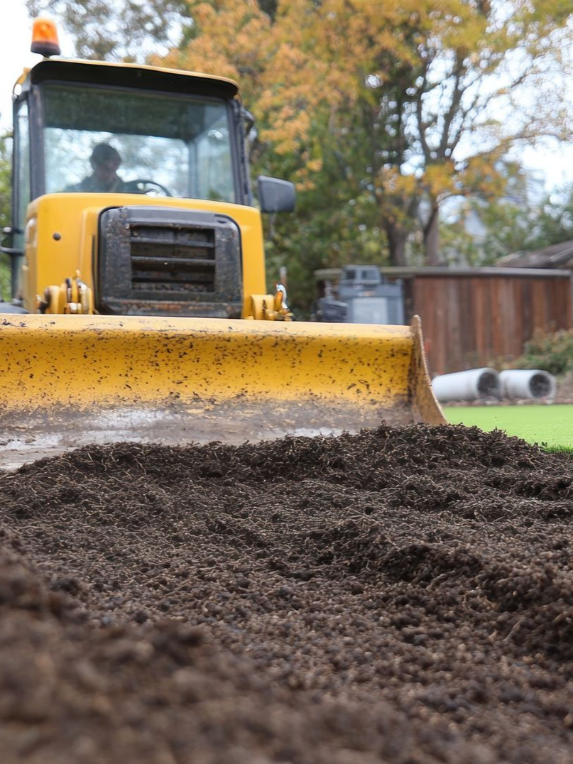 Bulldozer jaune poussant de la terre sur un chantier de construction ; une personne est dans la cabine.