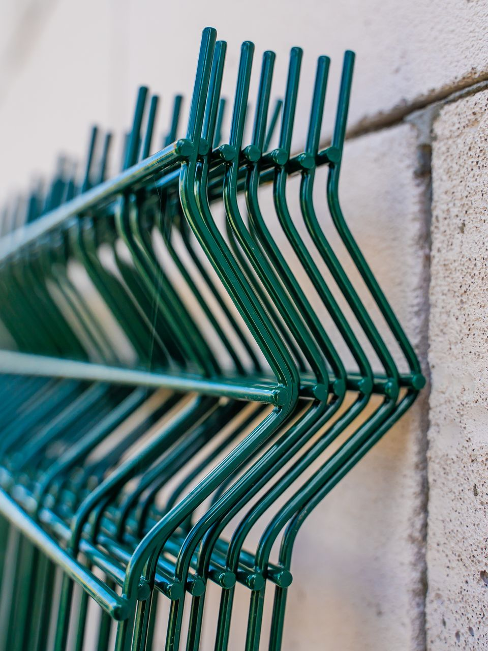 Clôture en fil de fer vert à motif en zigzag contre un mur de couleur neutre.