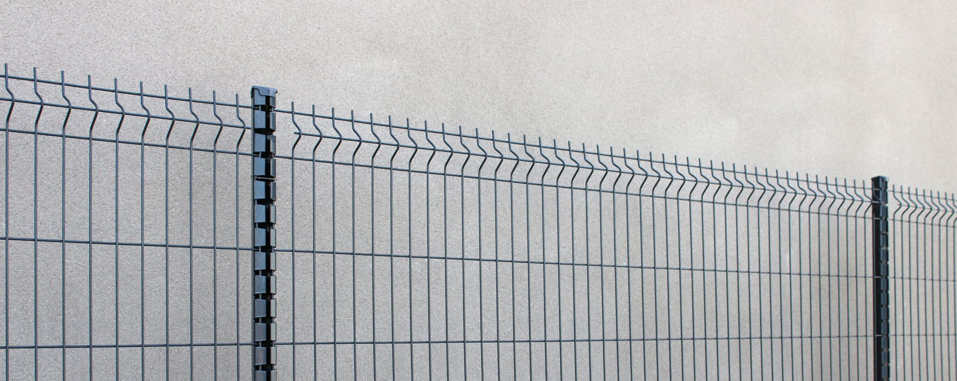 Clôture en treillis métallique contre un mur de couleur claire.