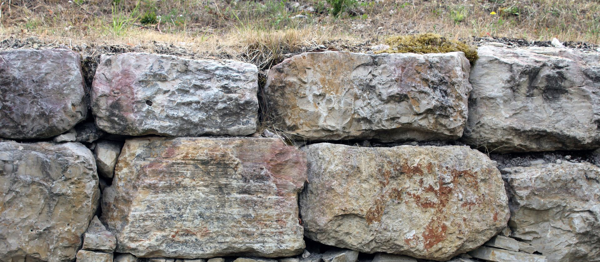 Mur de pierre en blocs rectangulaires bruts. Espace gazonné au-dessus.