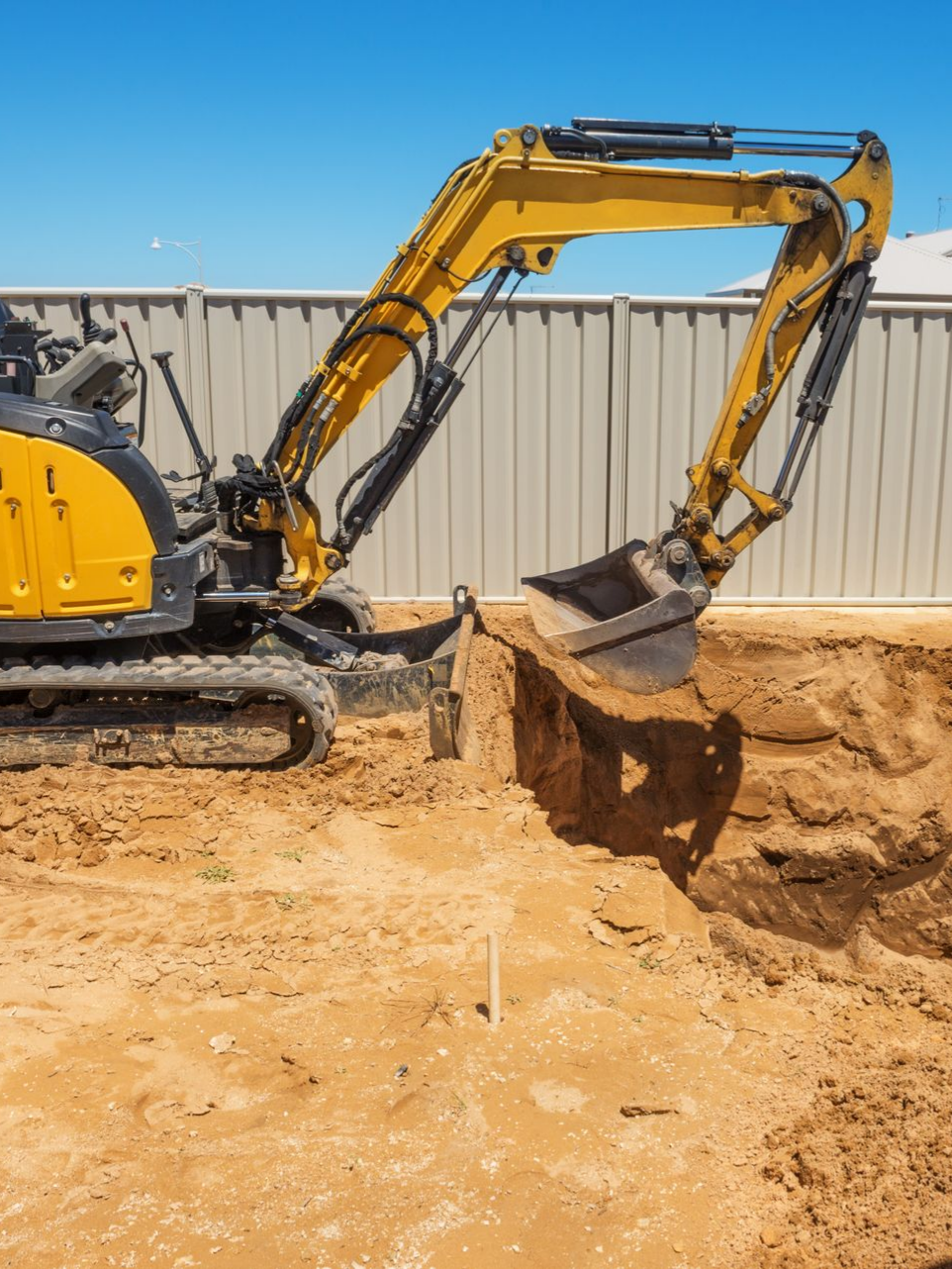 Excavatrice jaune creusant dans la terre par une journée ensoleillée.