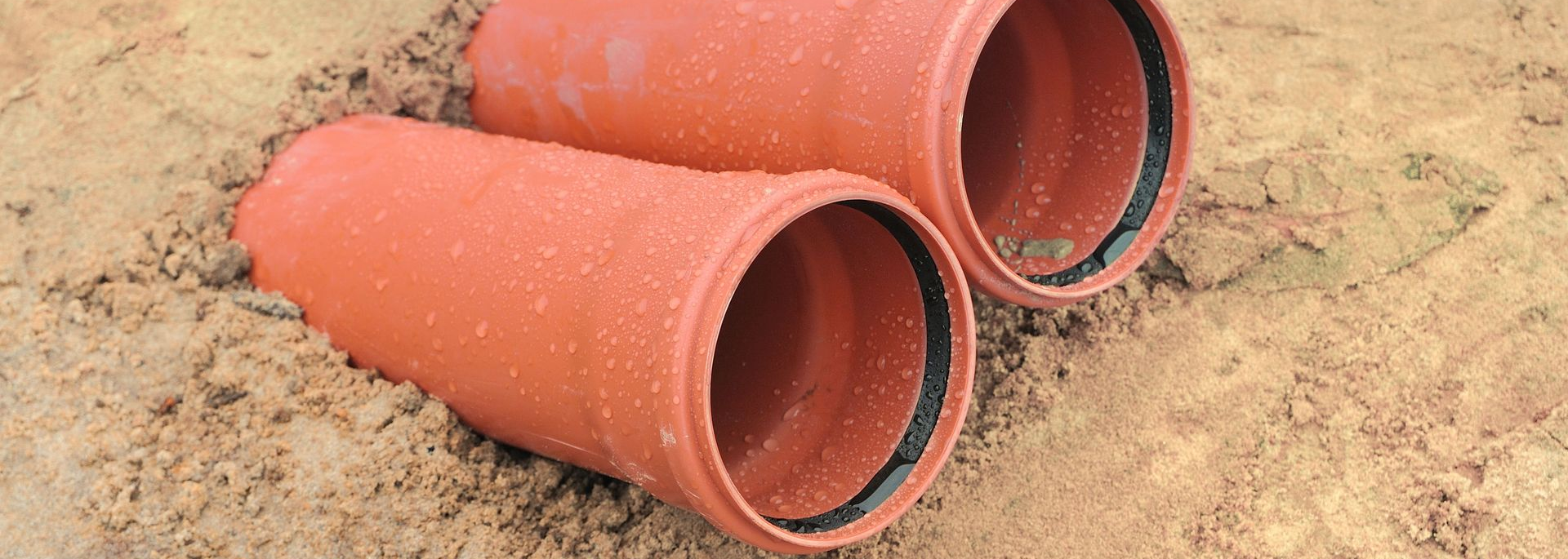 Deux tuyaux orange avec des anneaux noirs, posés dans le sable.