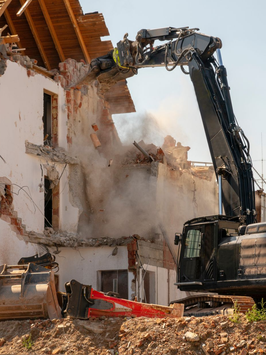 Démolition d'un bâtiment avec une excavatrice, volutes de poussière.