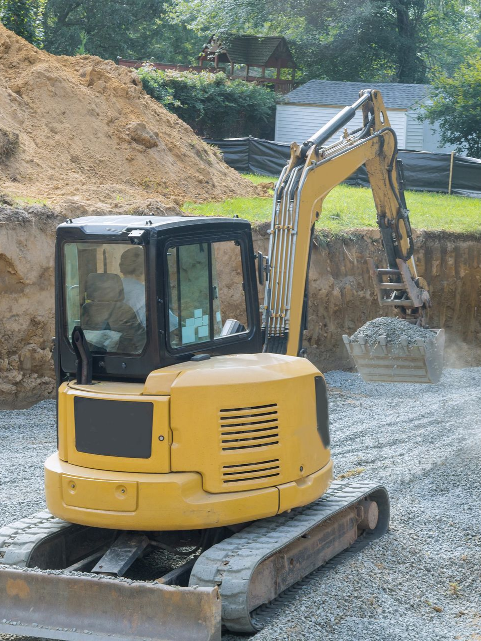 Une excavatrice jaune ramasse du gravier sur un chantier de construction, à côté d'un monticule brun.