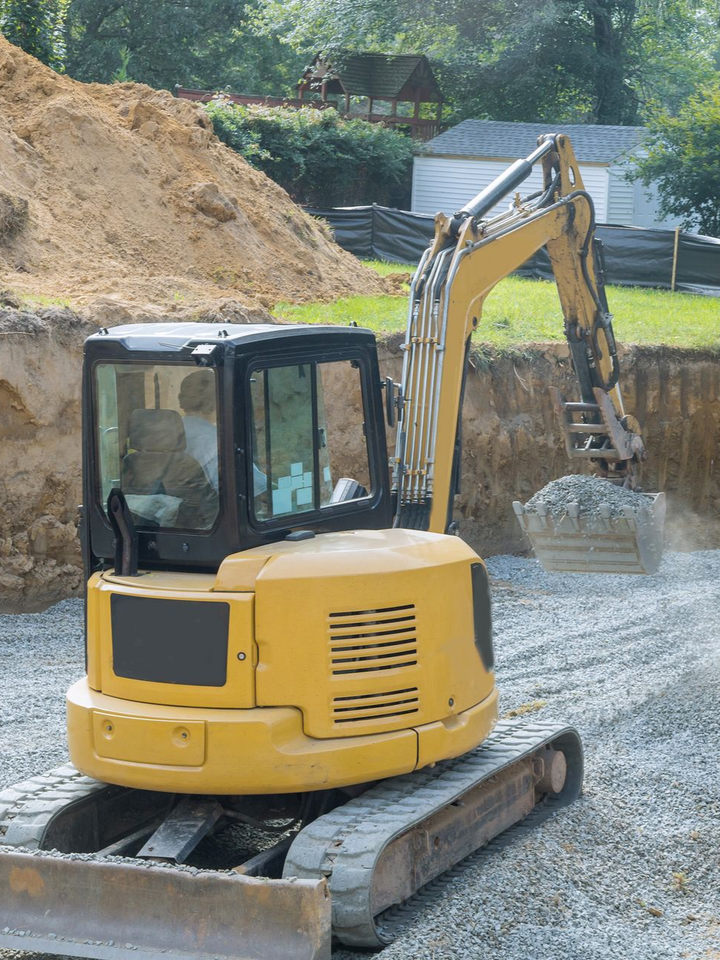 Une excavatrice jaune ramasse du gravier sur un chantier de construction, à côté d'un monticule brun.