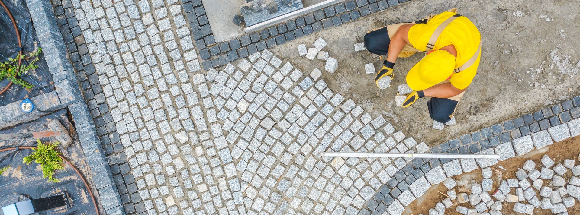 Une personne en vêtements de travail jaunes pose des pavés à l'extérieur.