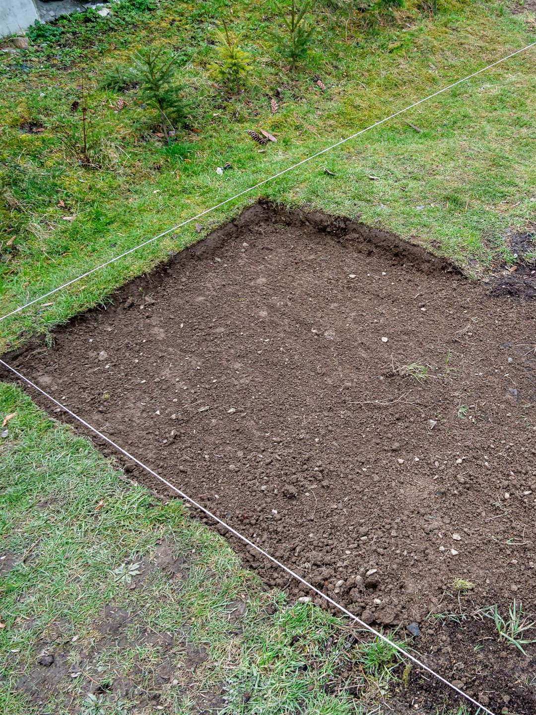 Un carré de jardin préparé dans une zone herbeuse, délimitée par une ficelle. La terre brune remplit le carré.