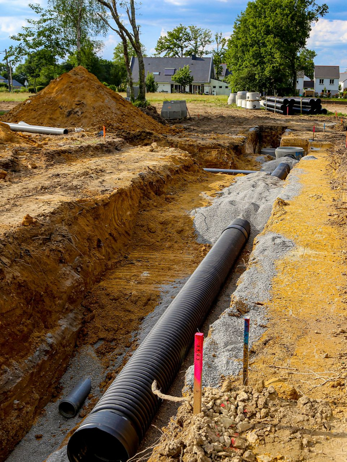 Chantier de construction avec un tuyau ondulé noir dans une tranchée, une base de gravier et de la terre environnante.