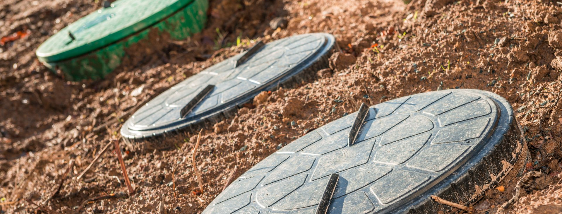 Trois couvercles d'accès au système d'irrigation enfouis dans la terre. L'un est vert, les deux sont gris.
