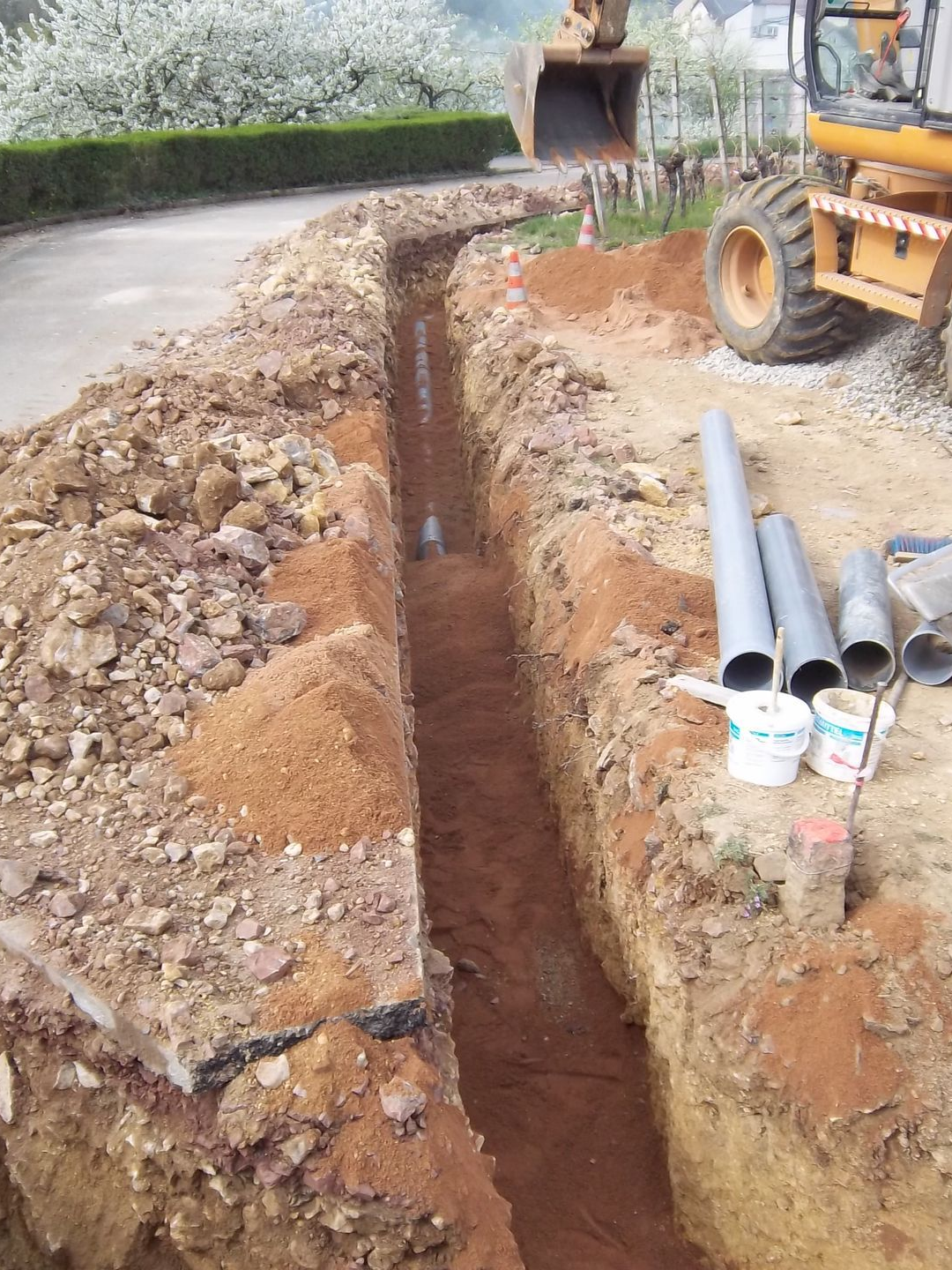 Excavatrice jaune creusant dans un monticule de terre, avec un paysage rural en arrière-plan.