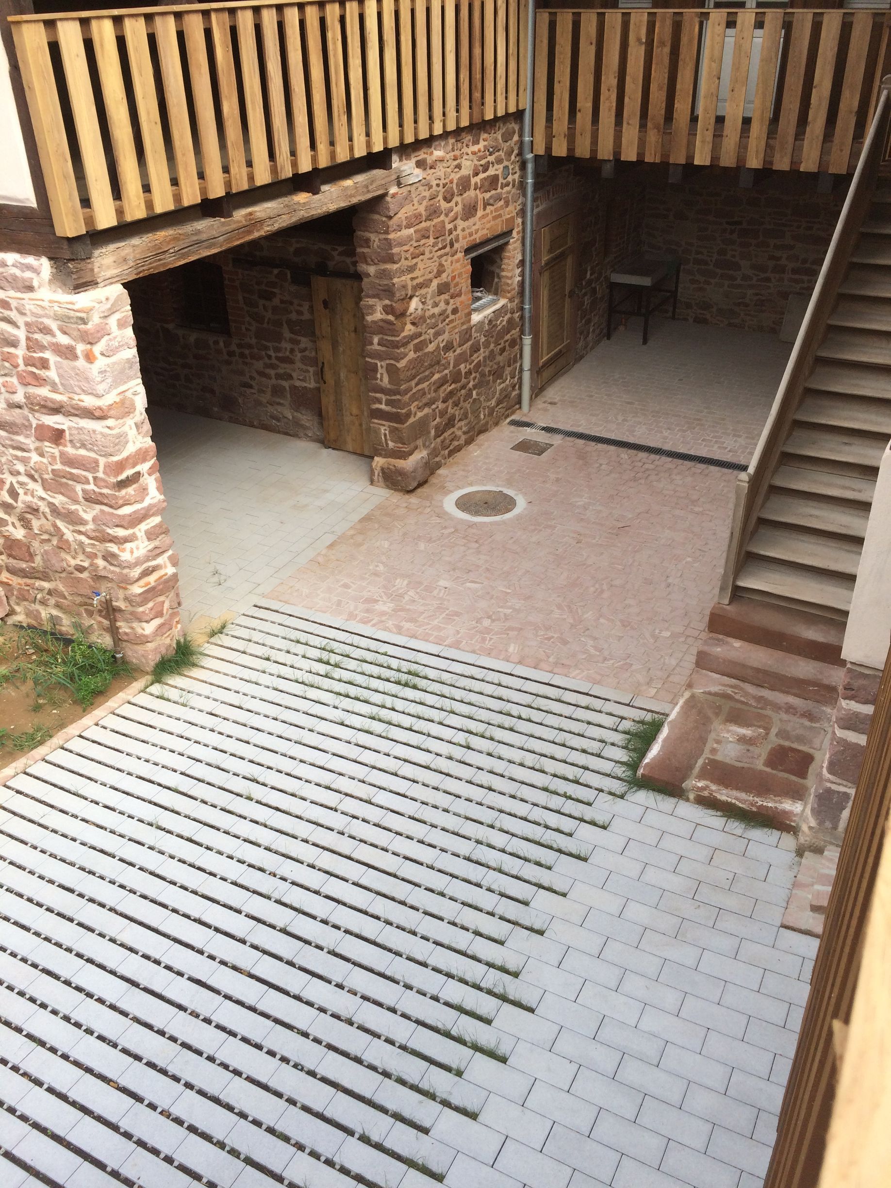 Cour avec murs en briques, balcons en bois et escaliers. Une allée pavée grise mène à l'entrée.