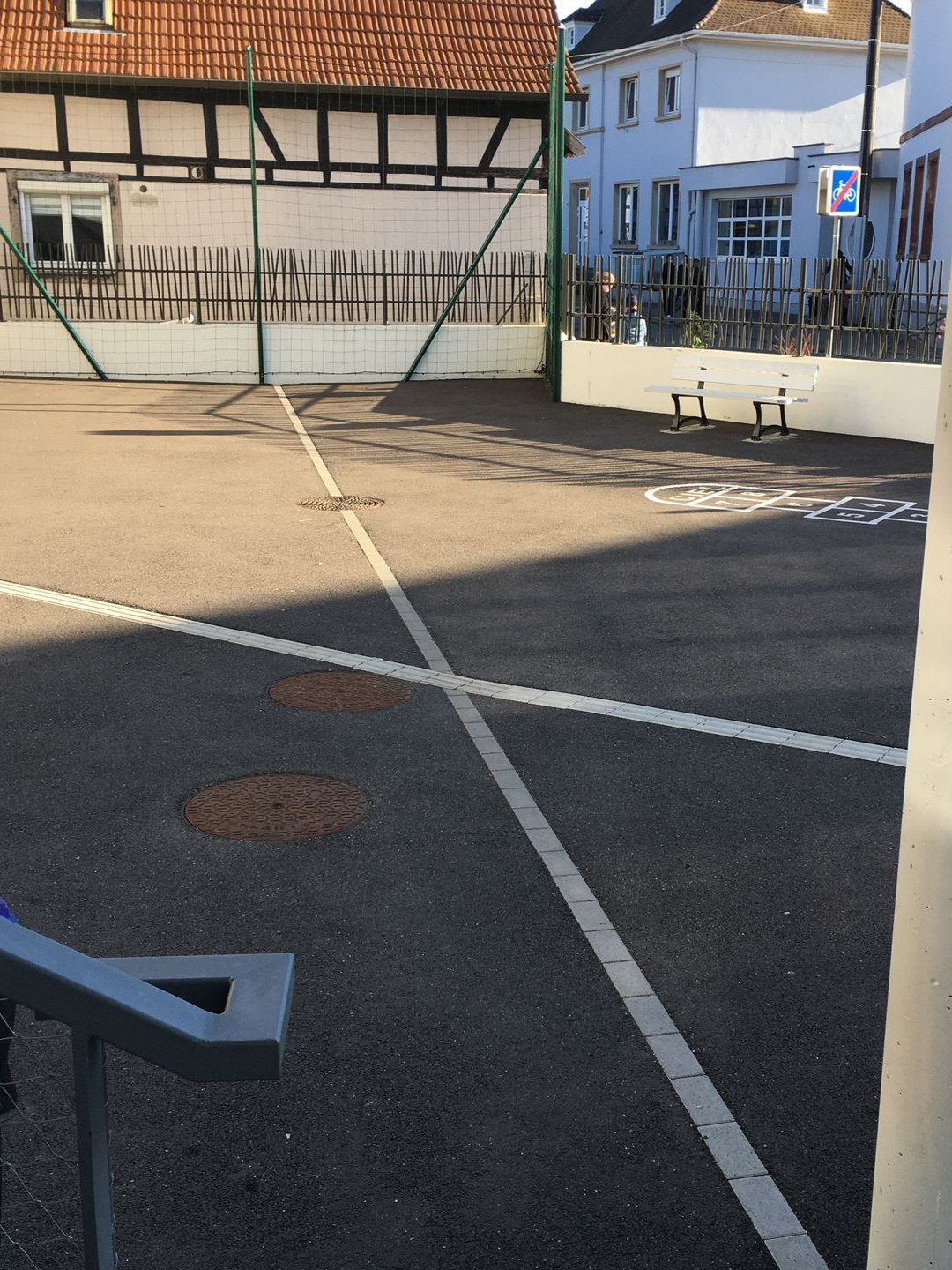 Aire de jeux avec des lignes blanches, des clôtures et des bâtiments en arrière-plan.