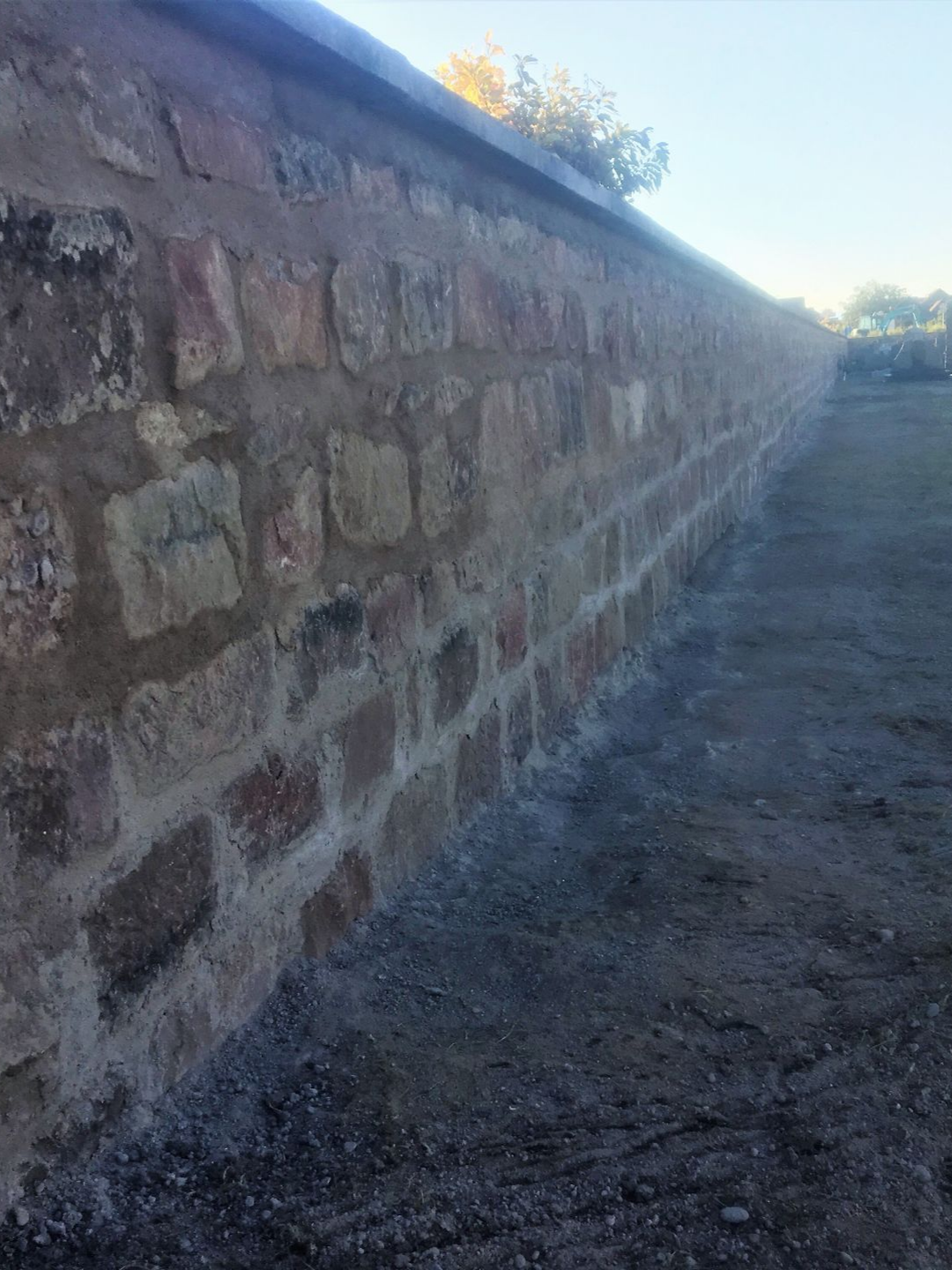 Mur de pierre avec mortier, le long d'un chemin de terre, sous un ciel clair.