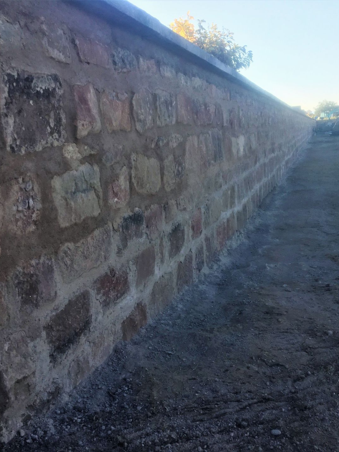 Mur de pierre avec mortier, longeant un sol sombre sous un ciel bleu.