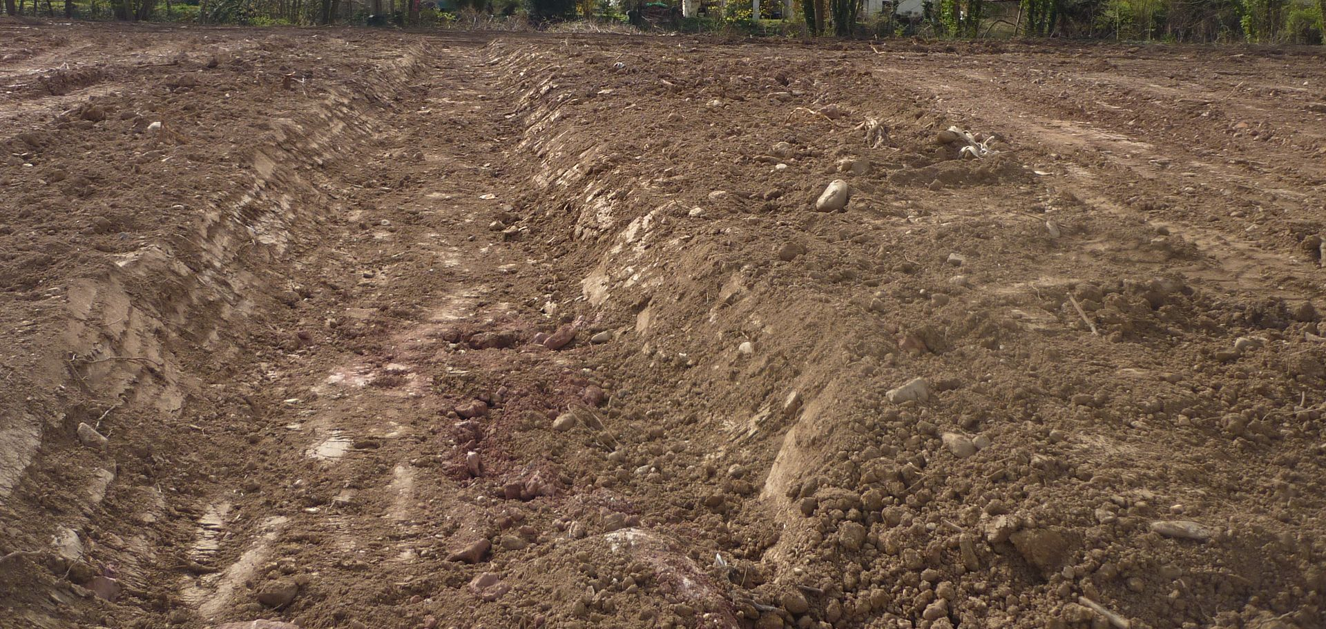 Un champ vide, brun et sale, peut-être labouré, sous un ciel clair.