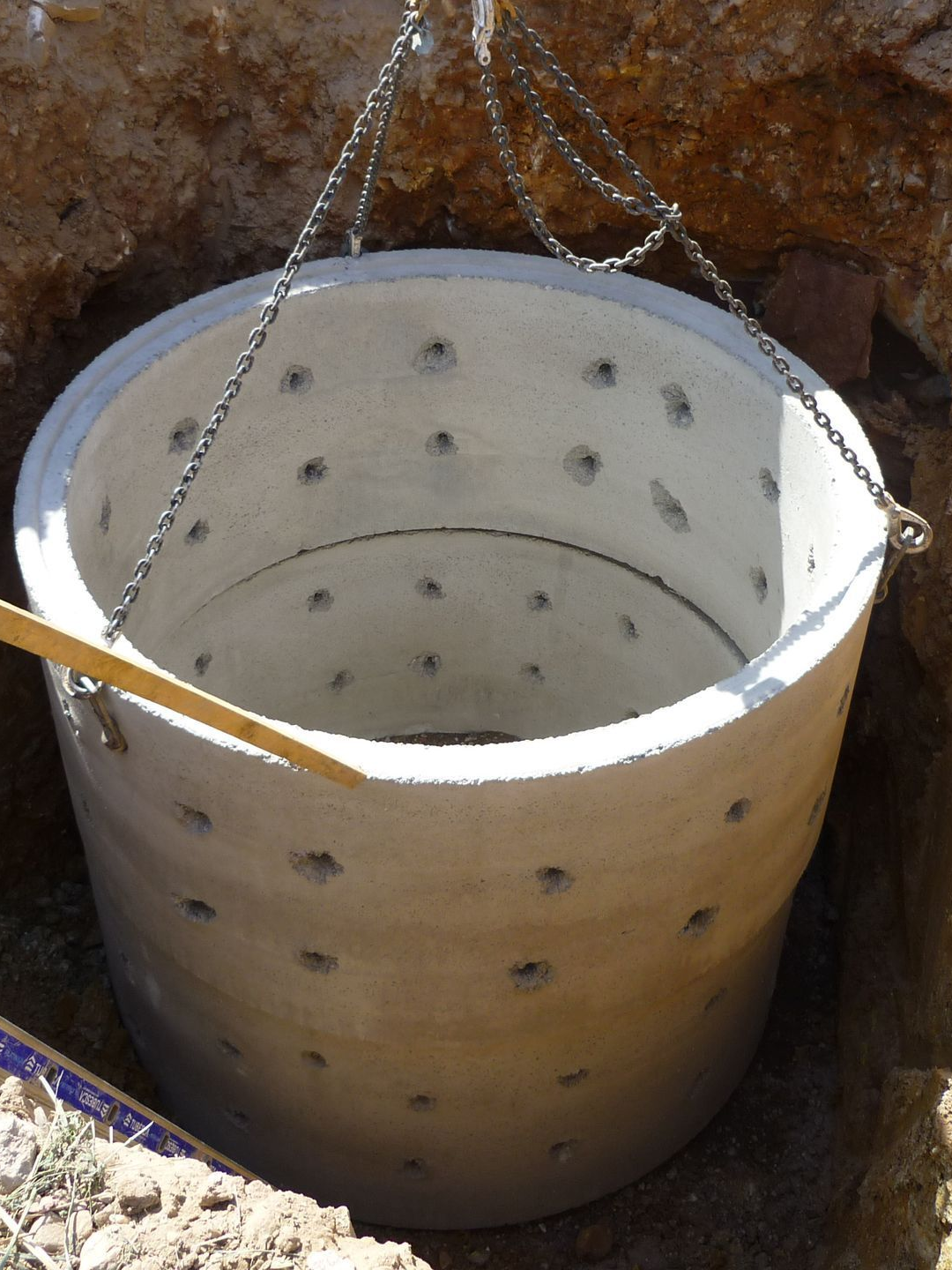 Anneau de puits en béton descendu dans un trou par des chaînes.
