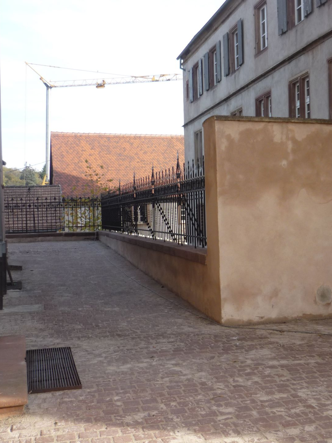 Cour en brique avec clôture en fer forgé, bâtiment et grue de chantier.
