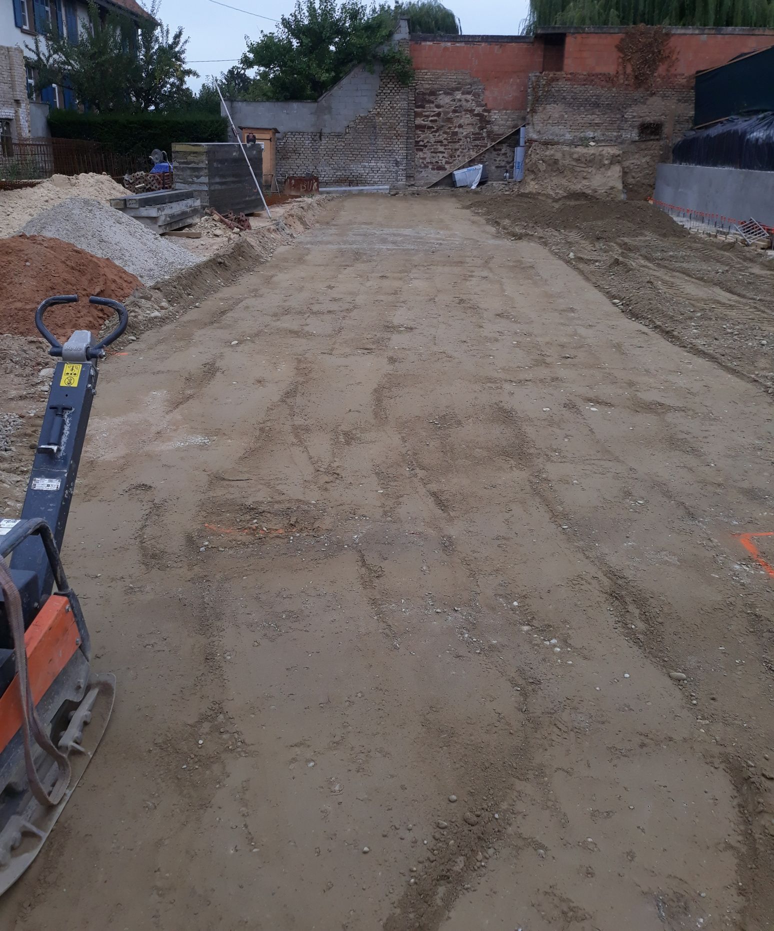 Chantier de construction avec une plaque vibrante sur terre compactée.