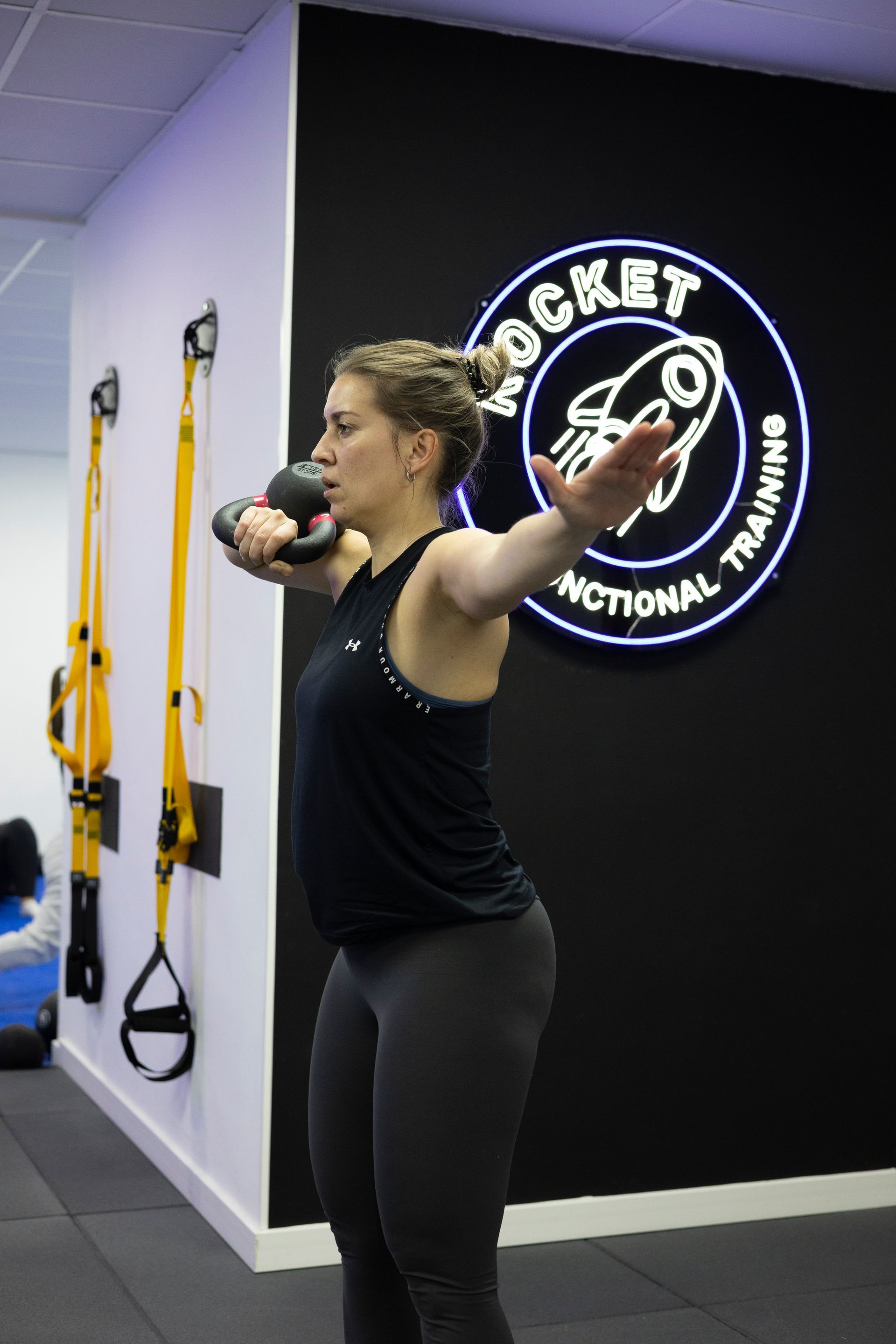 Una mujer está levantando una pesa rusa frente a un cartel que dice cohete.
