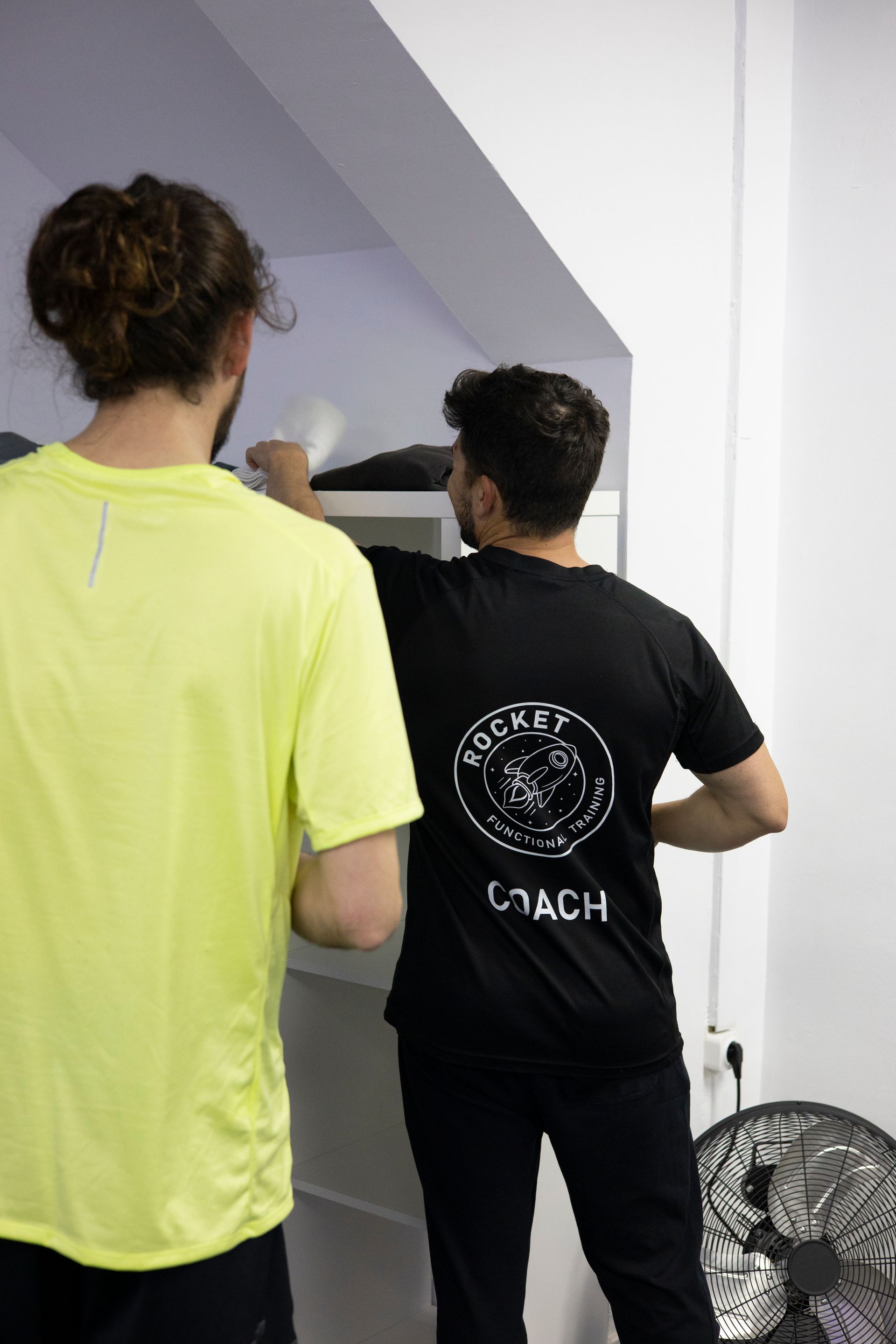 Dos hombres están parados uno al lado del otro en una habitación. Uno de los hombres lleva una camisa amarilla.