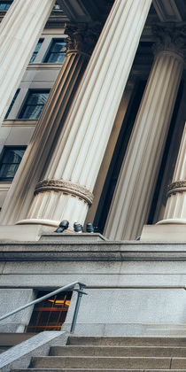 Façade d’un grand bâtiment en pierre, avec de hautes colonnes cannelées et un escalier menant à l’entrée
