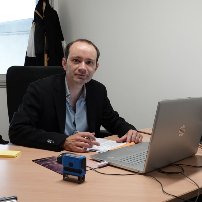 Réunion d’affaires entre deux hommes qui se serrent la main au-dessus d’un bureau, avec une balance de la justice posée sur la table.
