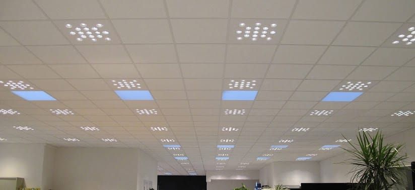 Techo de oficina con filas de luces LED brillantes y rejillas de ventilación sobre los escritorios y una planta en maceta.
