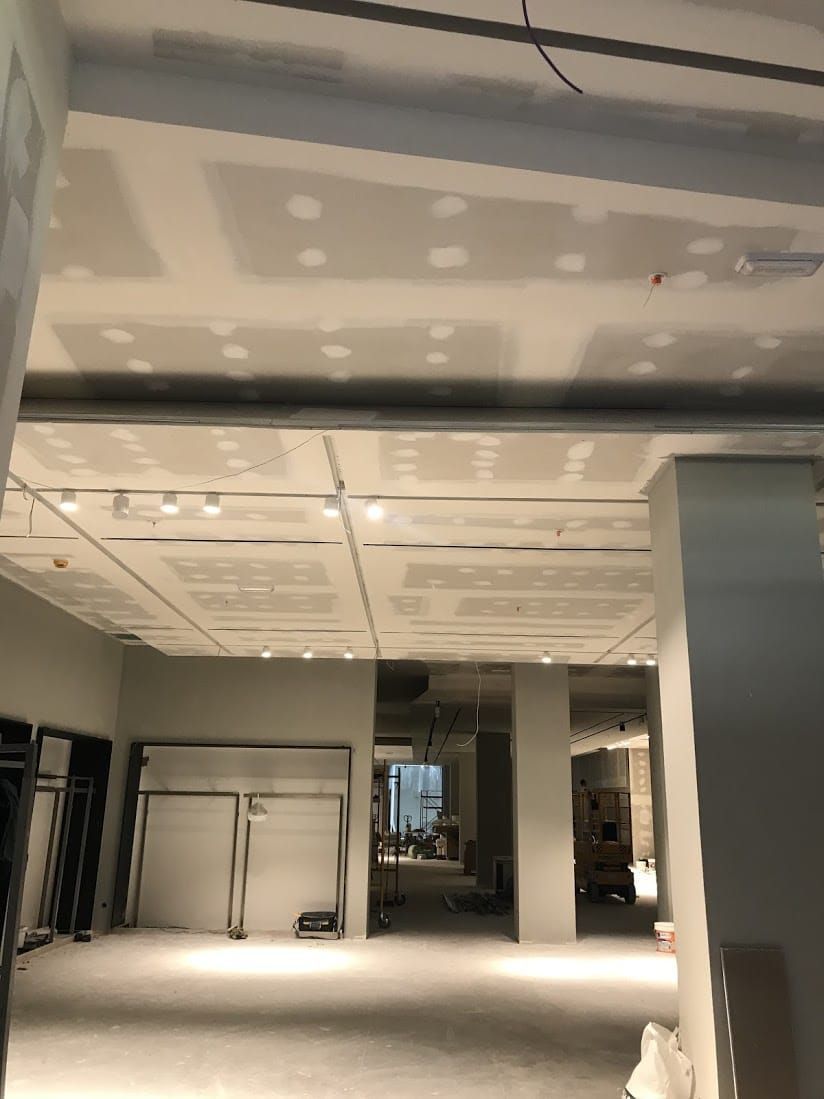 Interior vacío y sin terminar, con techo de pladur, columnas y materiales de construcción sobre un suelo desnudo.