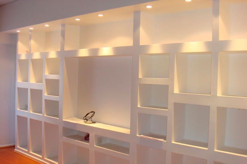 Estanterías blancas empotradas en la pared con iluminación cálida y un pequeño rincón de escritorio en un interior moderno.