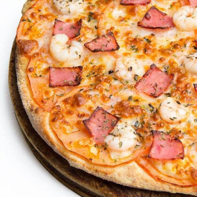 Una pizza con camarones, tocino y queso sobre una tabla de cortar de madera.