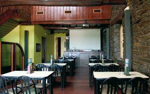 Un restaurante con mesas y sillas y una pantalla de proyección.
