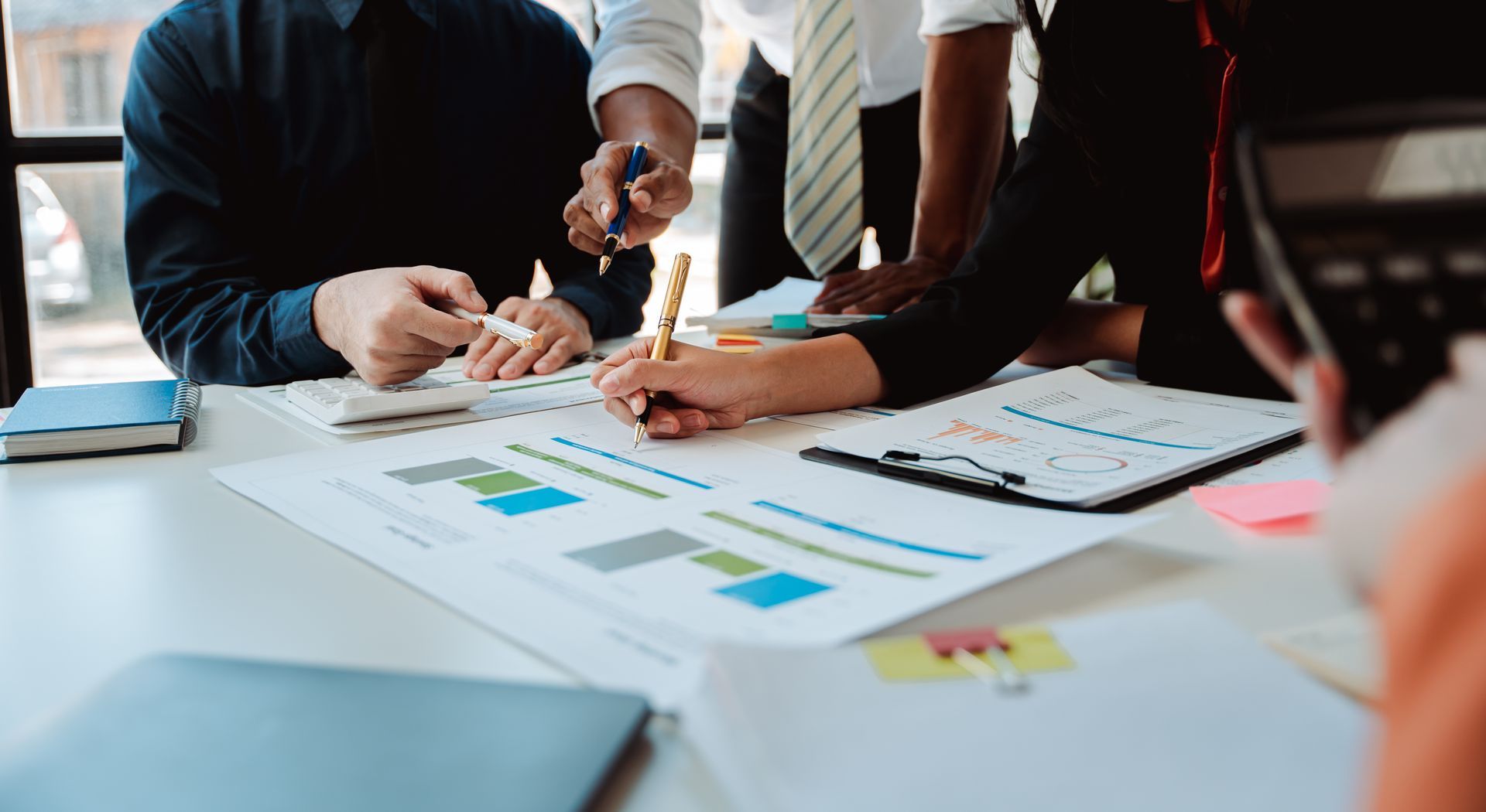 Das Business-Team arbeitet zusammen und analysiert Diagramme mit Stift und Taschenrechner am Schreibtisch.