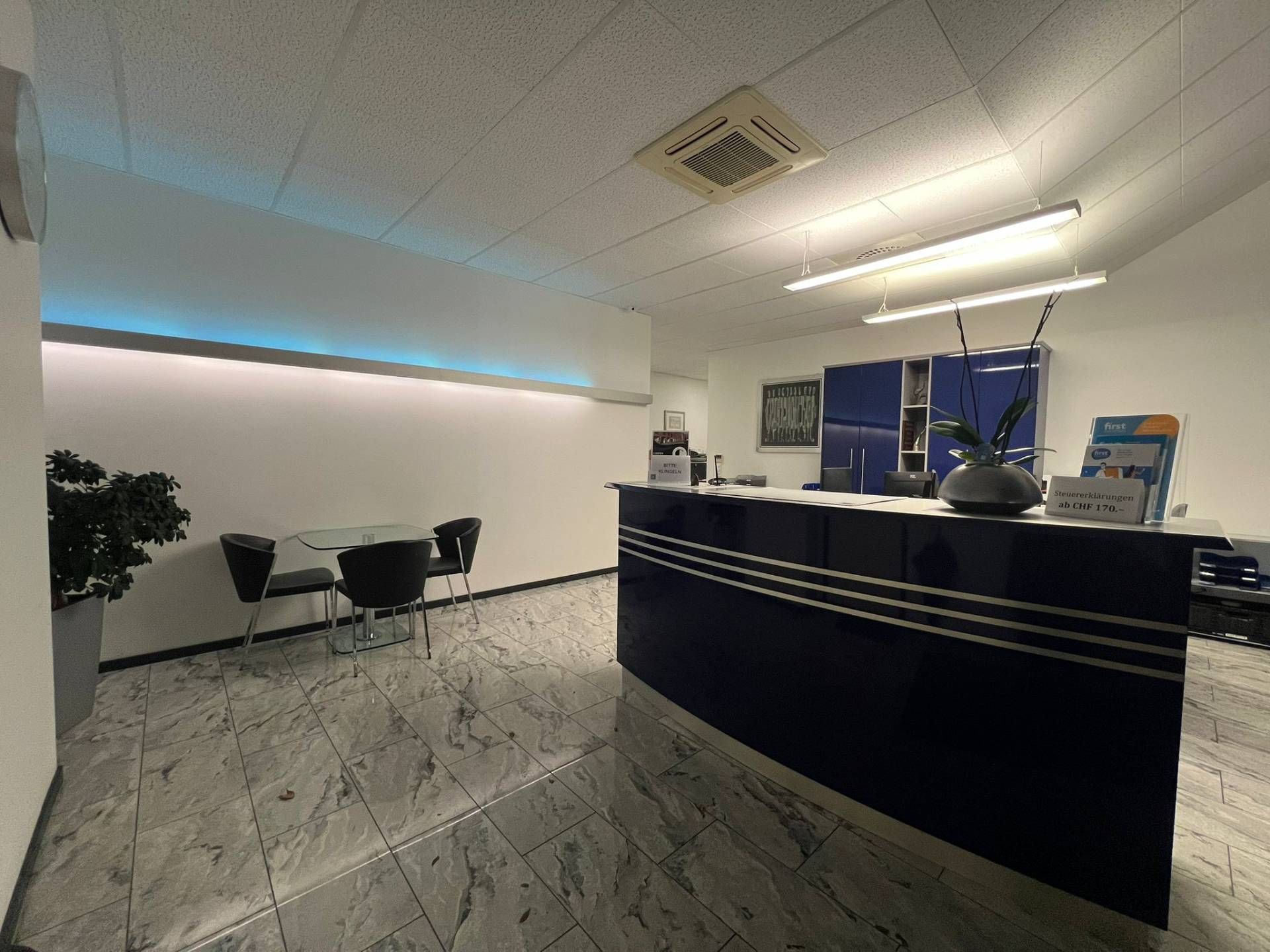 Empfangsbereich mit blauem Schreibtisch, Stühlen und Fliesenboden.