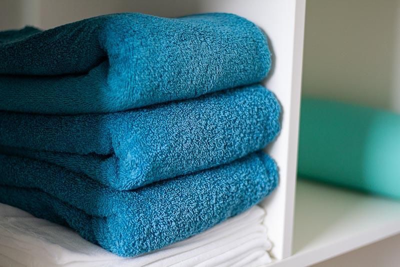 Drei blaue Handtücher liegen übereinander gestapelt auf einem Regal.