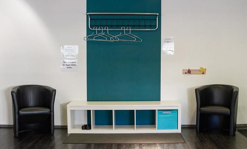 Ein Wartezimmer mit zwei Stühlen und einem Regal mit an der Wand hängender Kleidung.