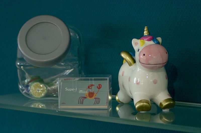 Eine Einhornfigur sitzt auf einem Glasregal neben einem Glas.