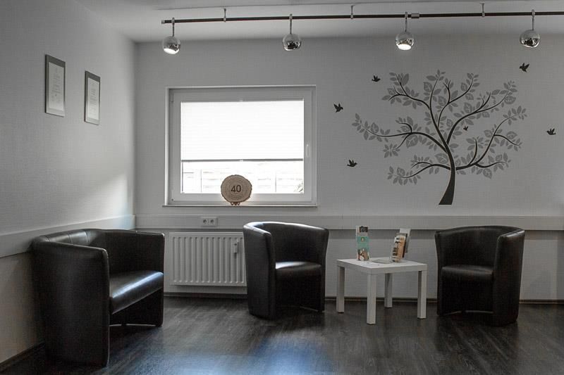 Ein Wartezimmer mit zwei Stühlen und einem Tisch mit einem Baum an der Wand.