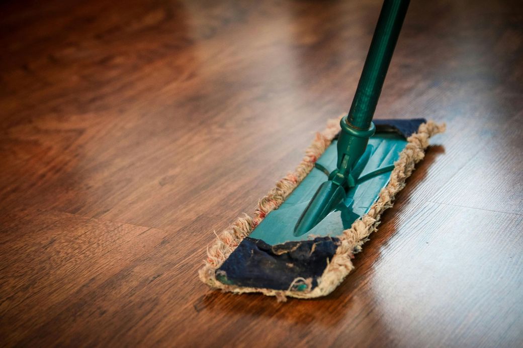 Une personne nettoie un plancher en bois avec une serpillière.