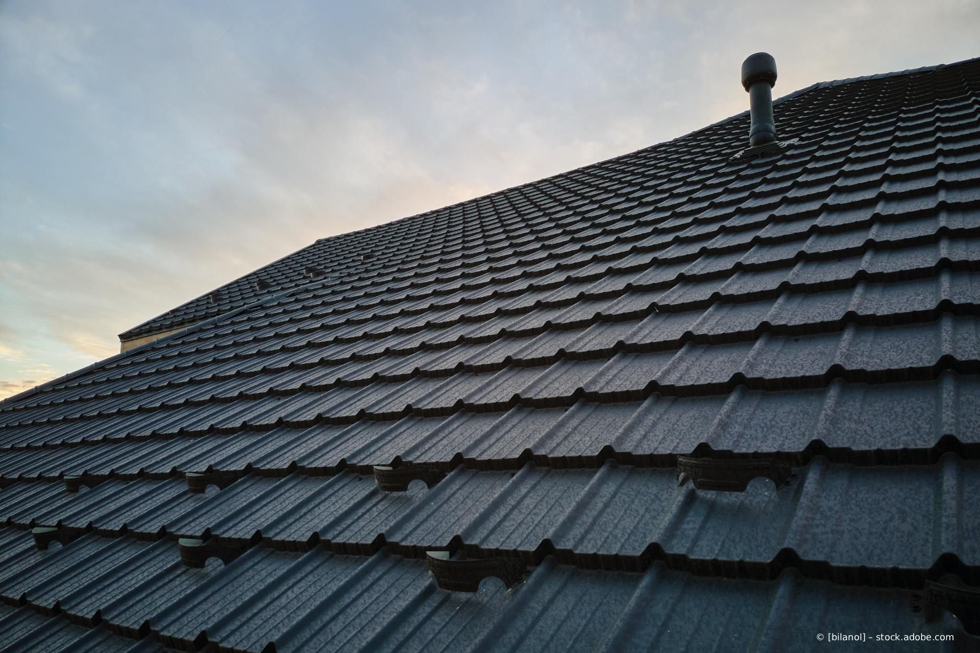 Dunkelgraues Ziegeldach mit einem Dachfenster und Schornstein vor einem bewölkten Himmel