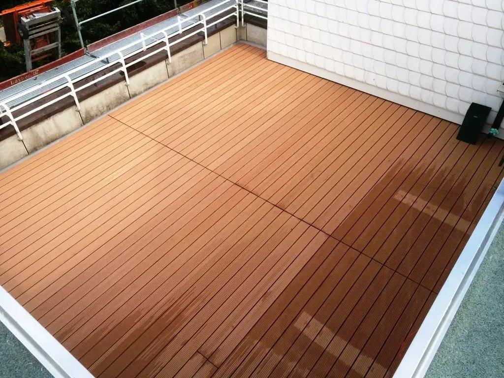 Holzterrasse auf dem Dach mit braunen Dielen, weißem Geländer und gefliester Wand in einem kleinen Außenbereich